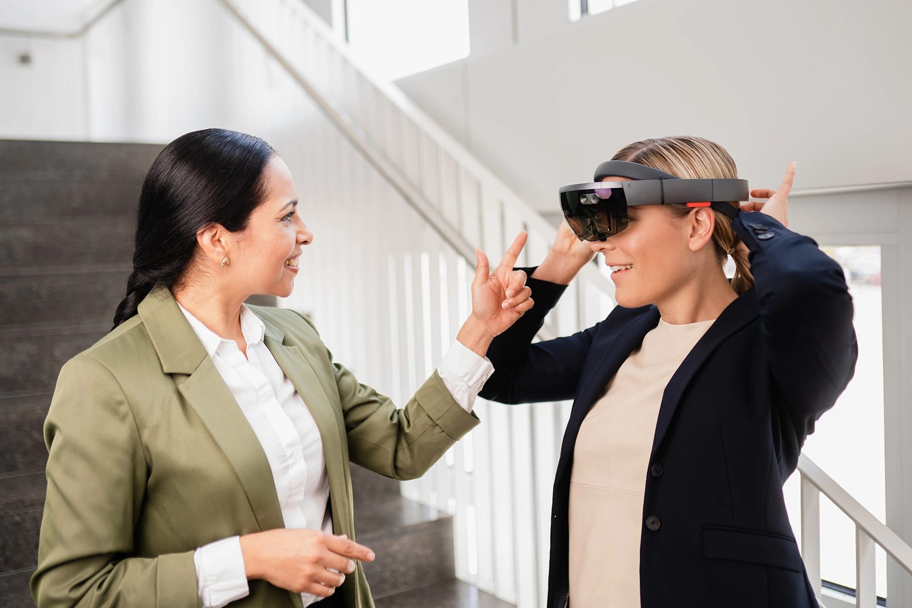 Dos compañeras conversan en una escalera mientras una de ellas se prueba unas gafas de realidad mixta.
